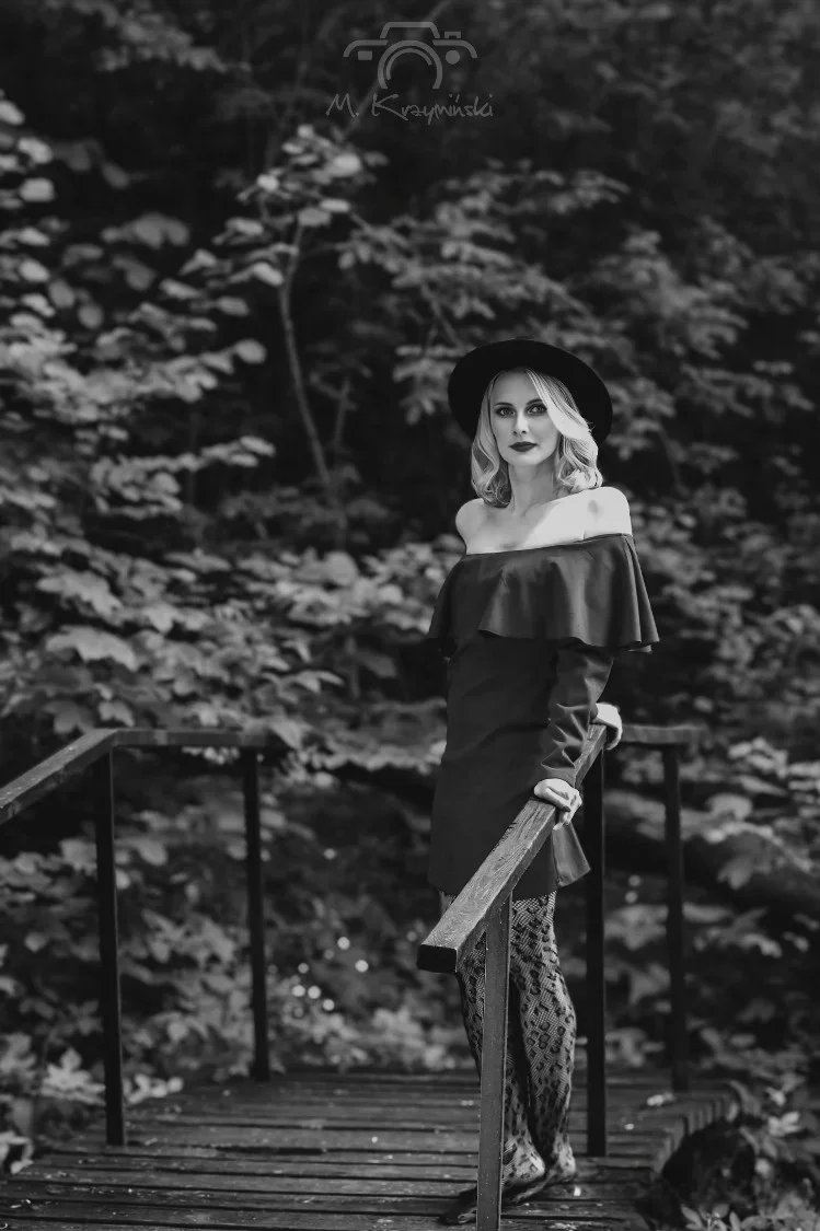 Z kapeluszem nasuniętym na głowę, lekko opierając się o drewnianą poręcz mostku. Była jak sen o minionym lecie, utkany z elegancji i cichej nostalgii.